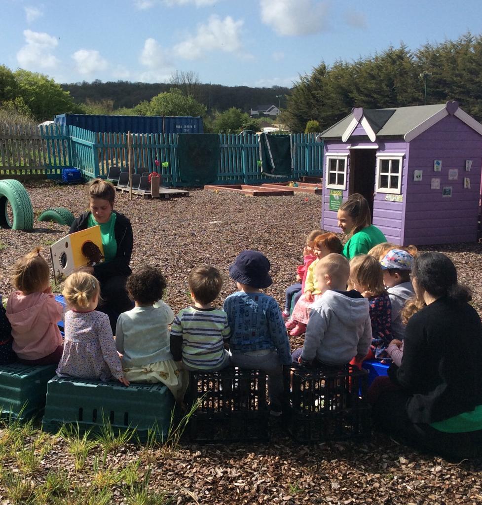 A group of children with two child carers reading to them outside
