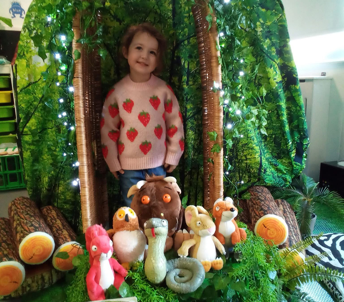 A young child standing and smiling with a group of teddies